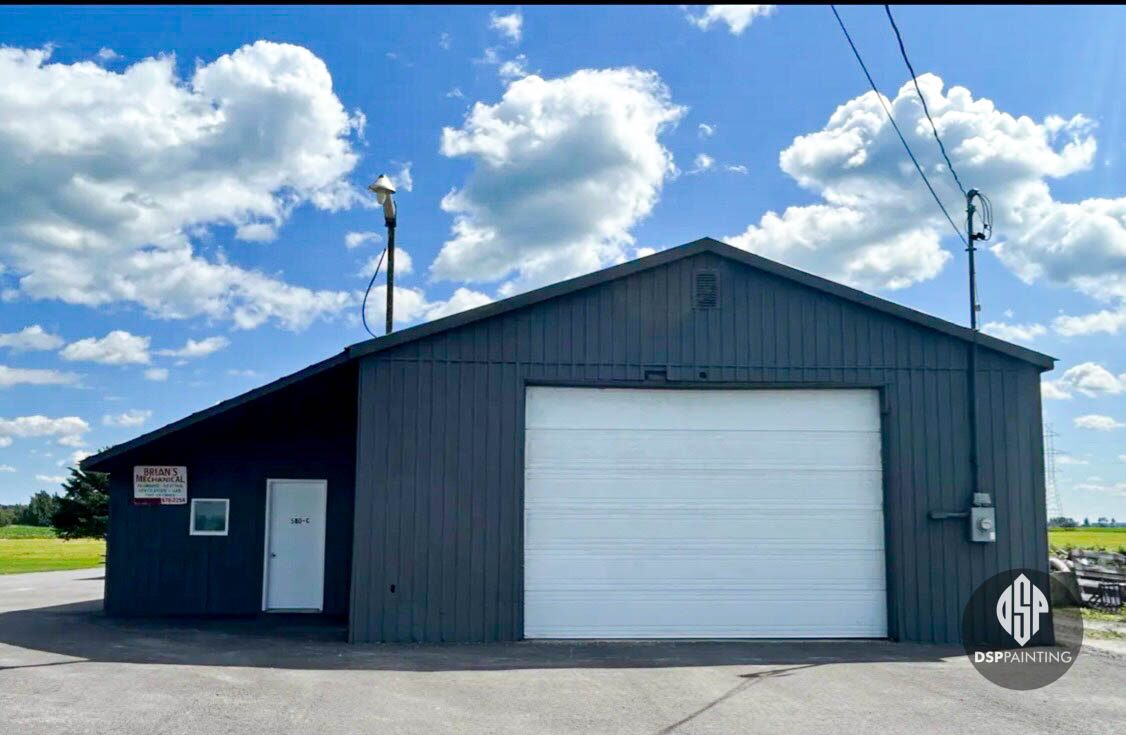 Repainted steel garage in dark grey, with a white overhead door and white service door, seen from the yard