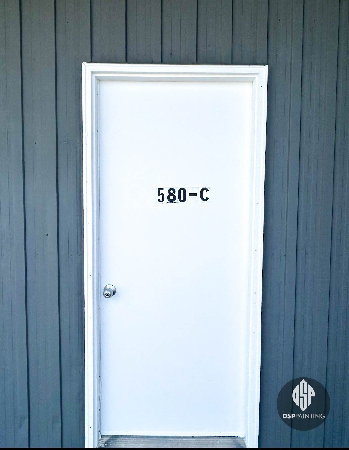 Close-up of the service door after painting, gloss white against the grey ribbed steel siding