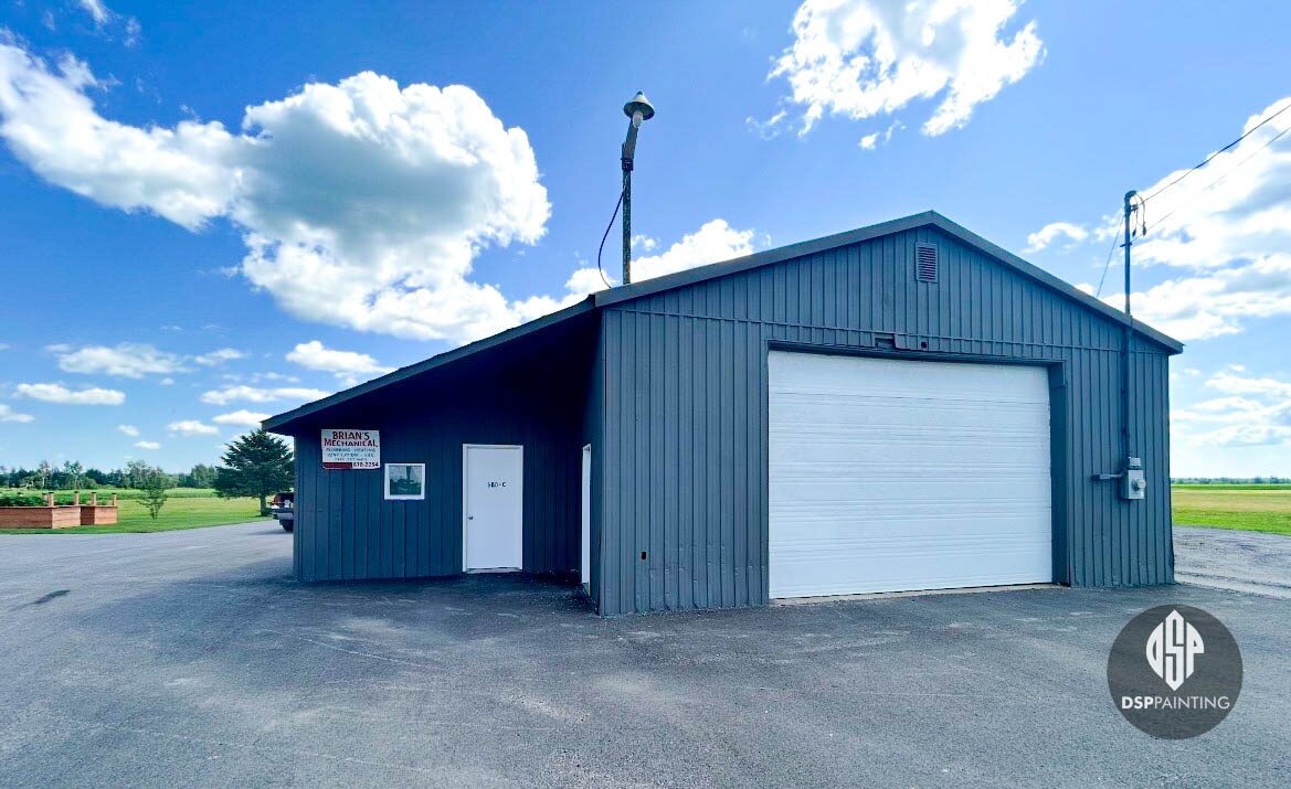 Detached steel-clad garage painted slate grey, with a white overhead door and white side entry door