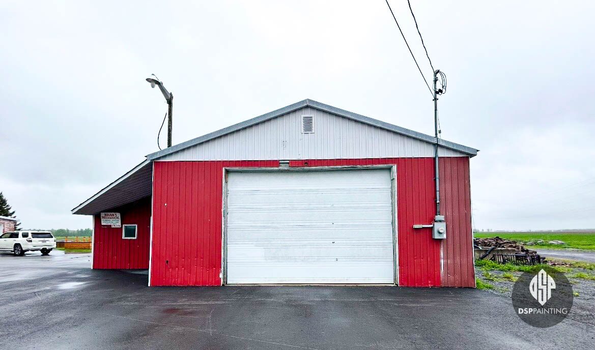 The garage before painting, weathered red siding below a bare white gable and rusted overhead door track
