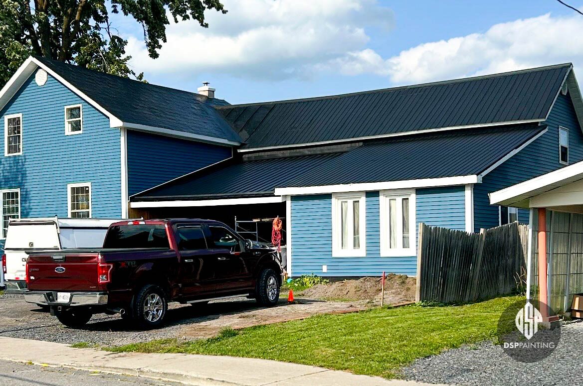 A blue country house and attached barn with their long metal roof painted black