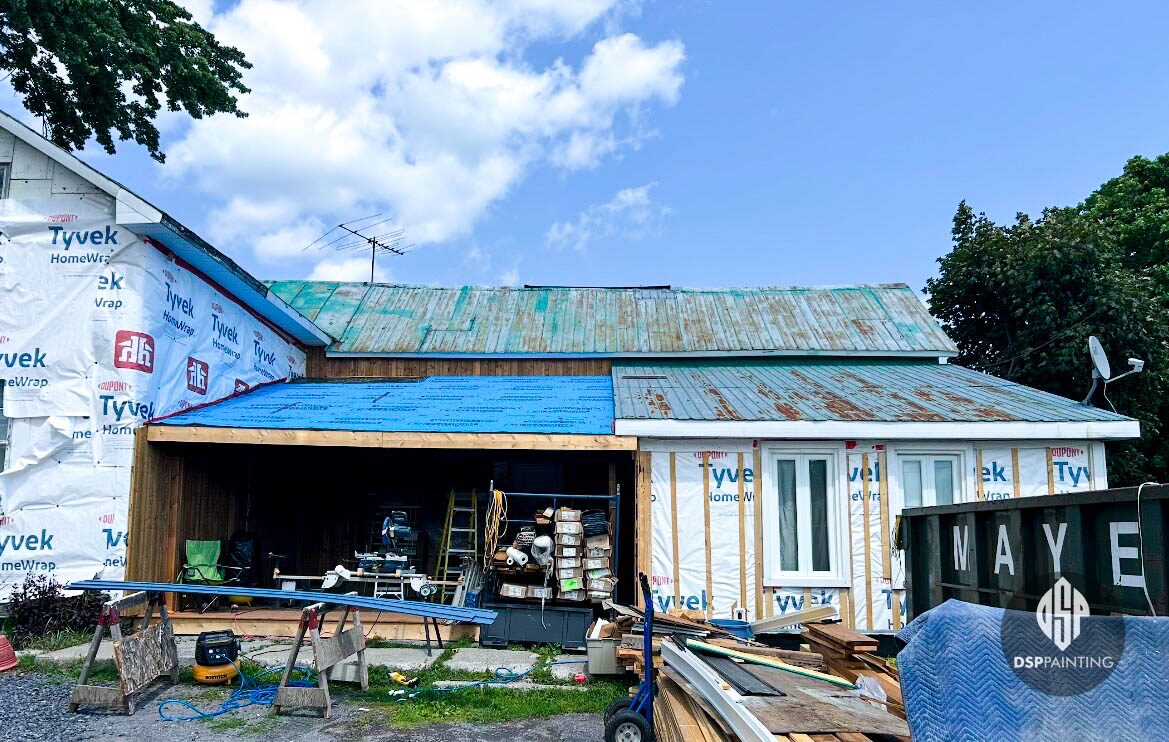 The roof before any work, rusted patched metal above walls still in house wrap