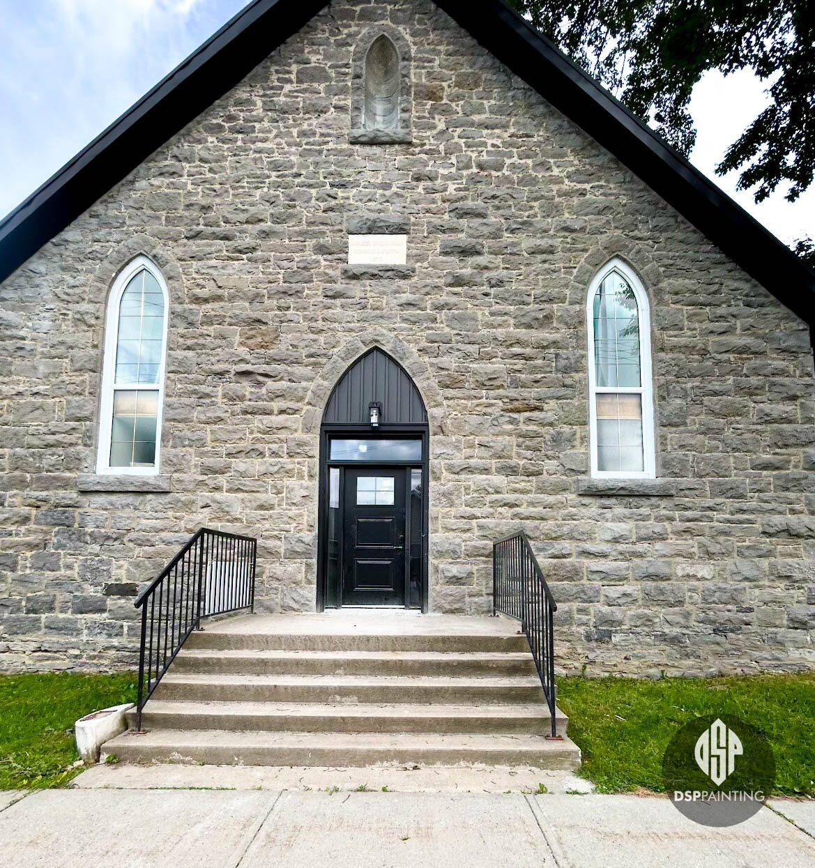 Front of the converted stone church, arched entry door painted black between white-framed gothic windows
