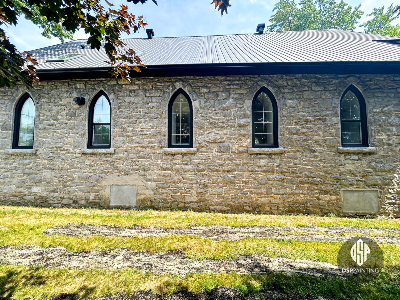 Converted stone church with tall arched windows in freshly painted dark frames, under a dark metal roof