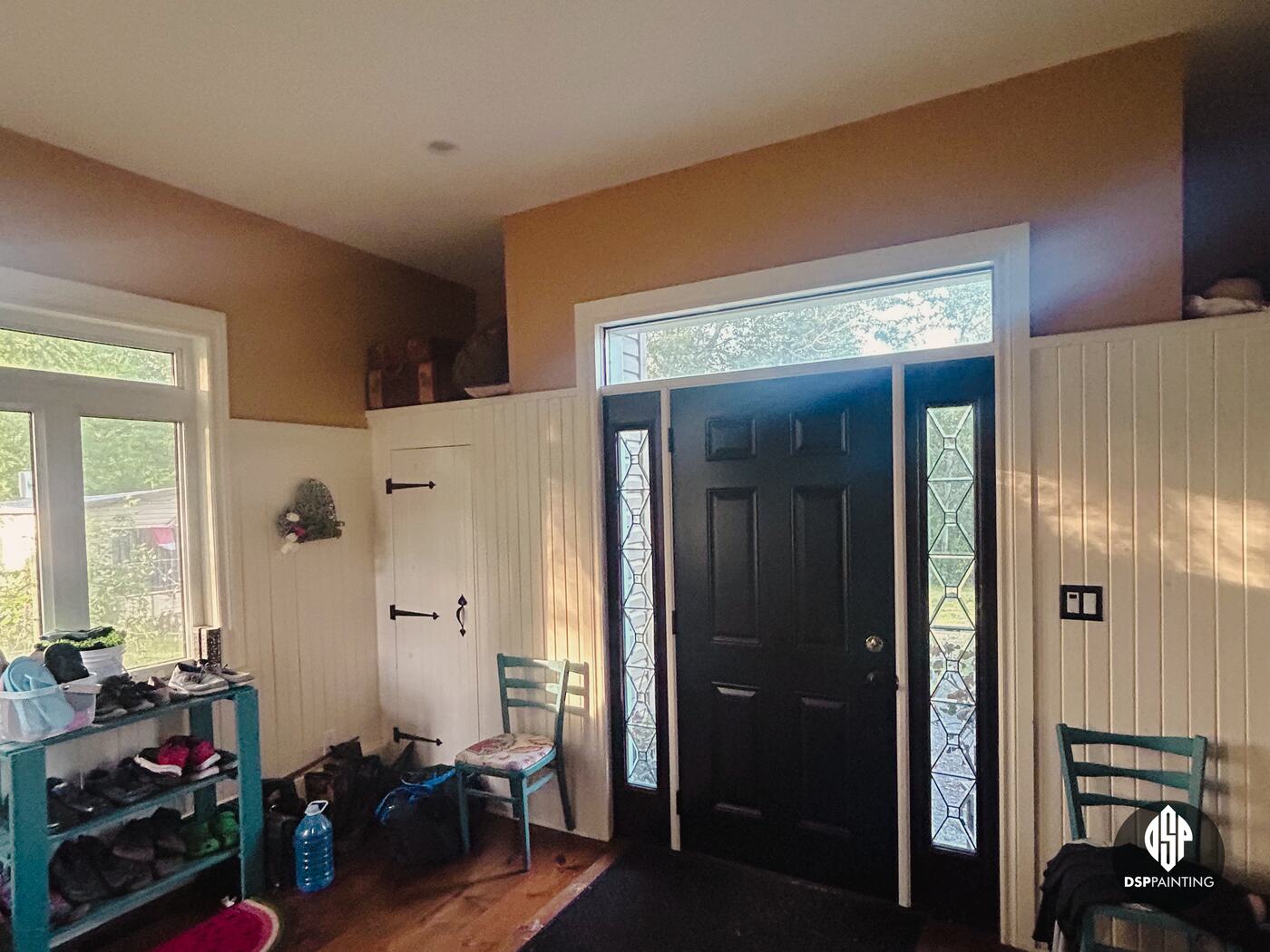 The front foyer before painting, tan upper walls above cream board panelling, beside the black front door and leaded sidelights