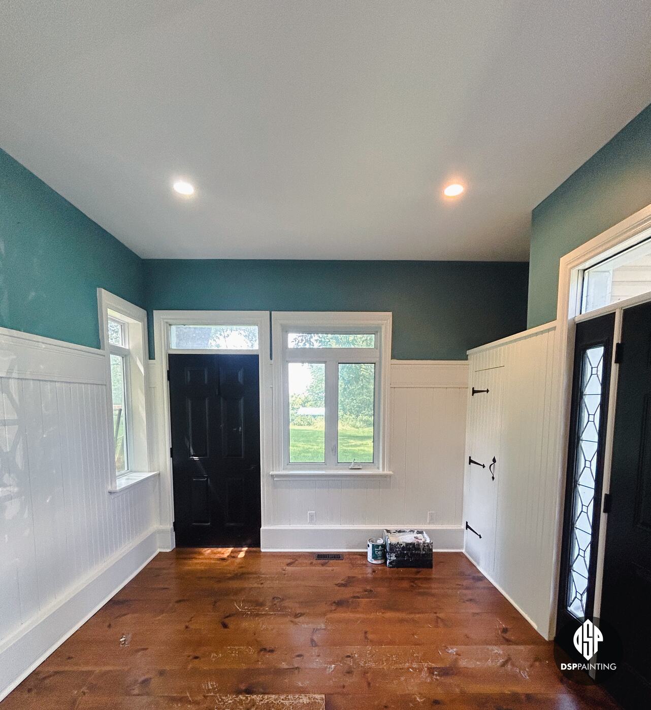 The finished foyer, teal upper walls and a white ceiling above white beadboard wainscoting, with both exterior doors in black