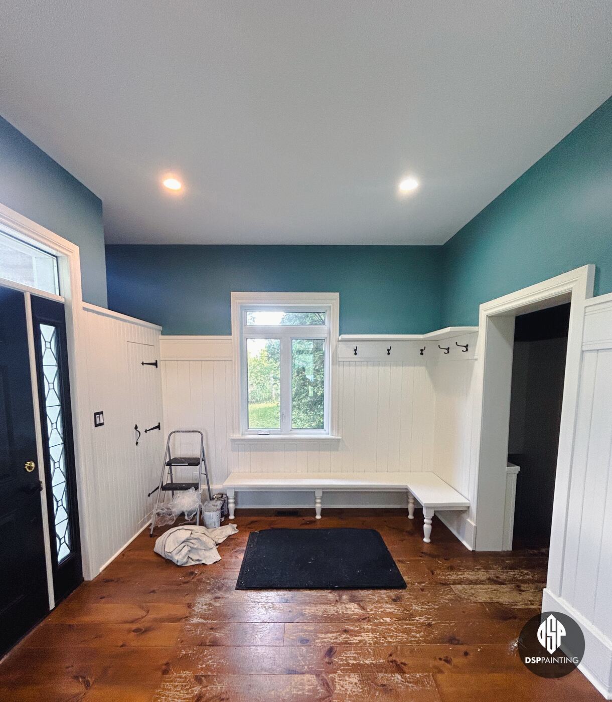 The other side of the foyer after painting, the white corner bench, coat hooks and doorway to the stairs under teal walls