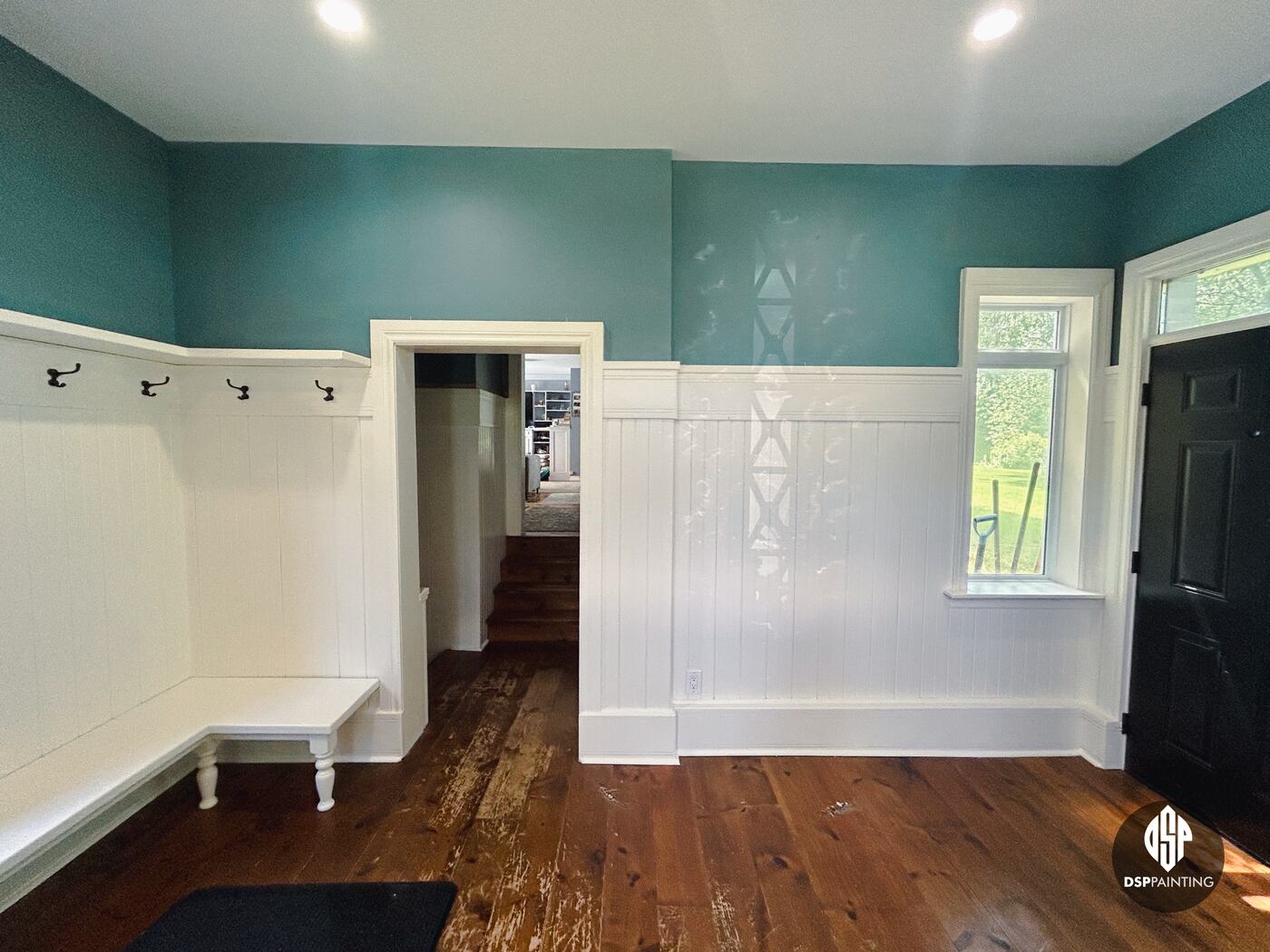 A wide view of the painted foyer, teal walls over white wainscoting from the corner bench to the black front door