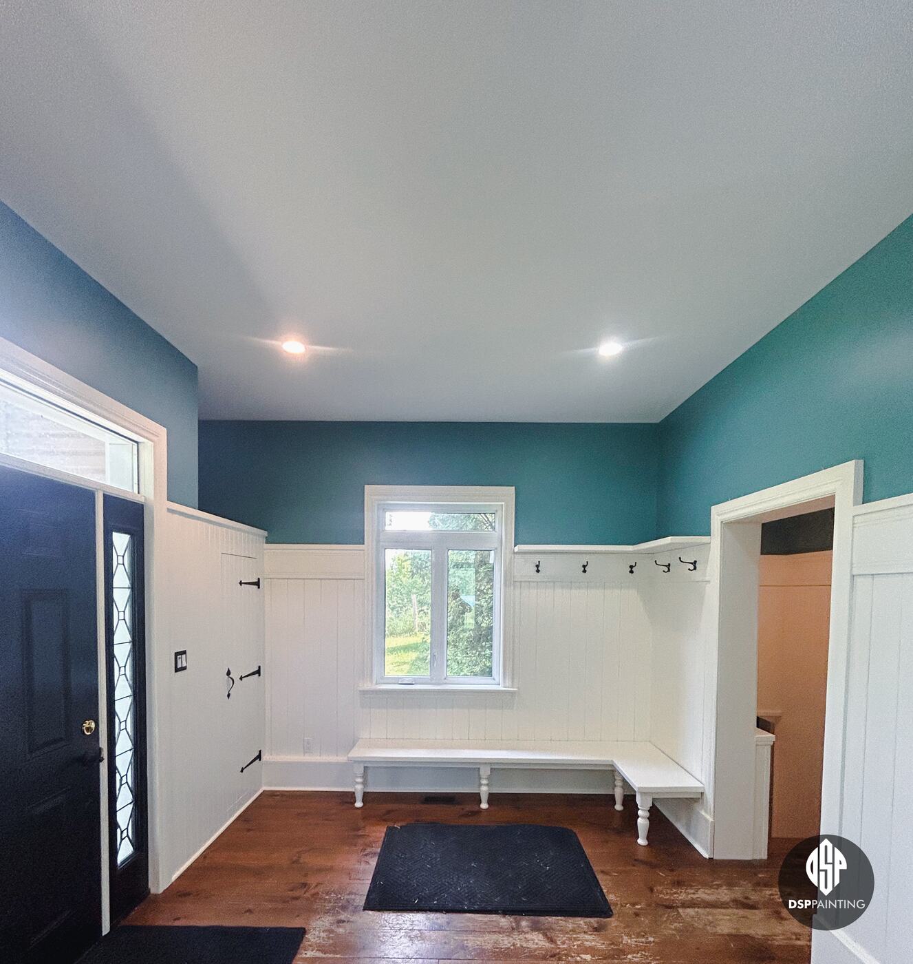 The white corner bench and coat-hook rail under the window, with the black front door on the left