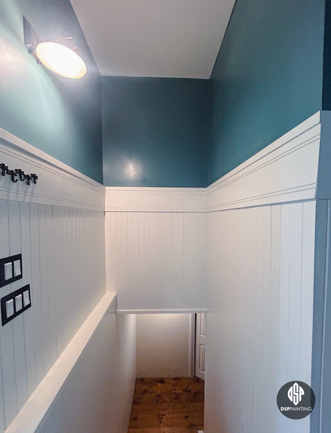 The stairwell after painting, teal walls above white panelling and trim, running down to the basement stairs