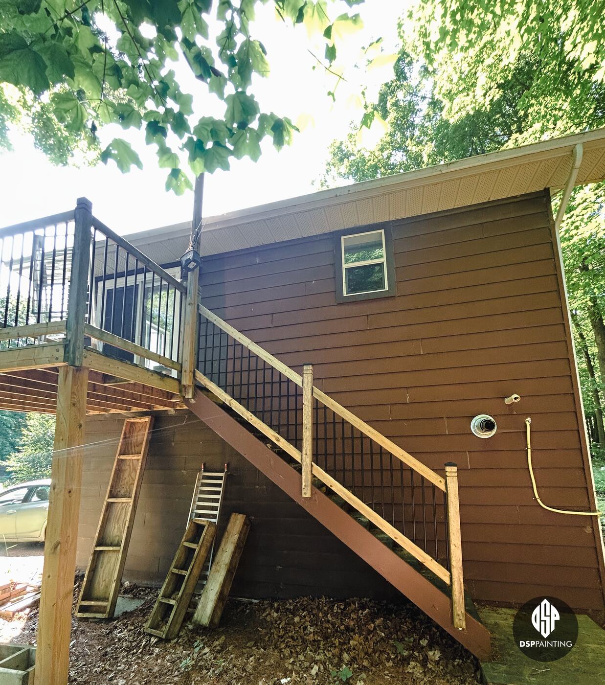 The back of the garage, red-brown siding behind the wooden stairs up to the second-floor deck