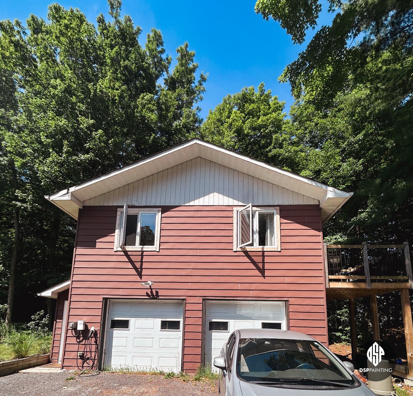 The front of the two-storey garage, red siding around two white overhead doors and the upstairs windows