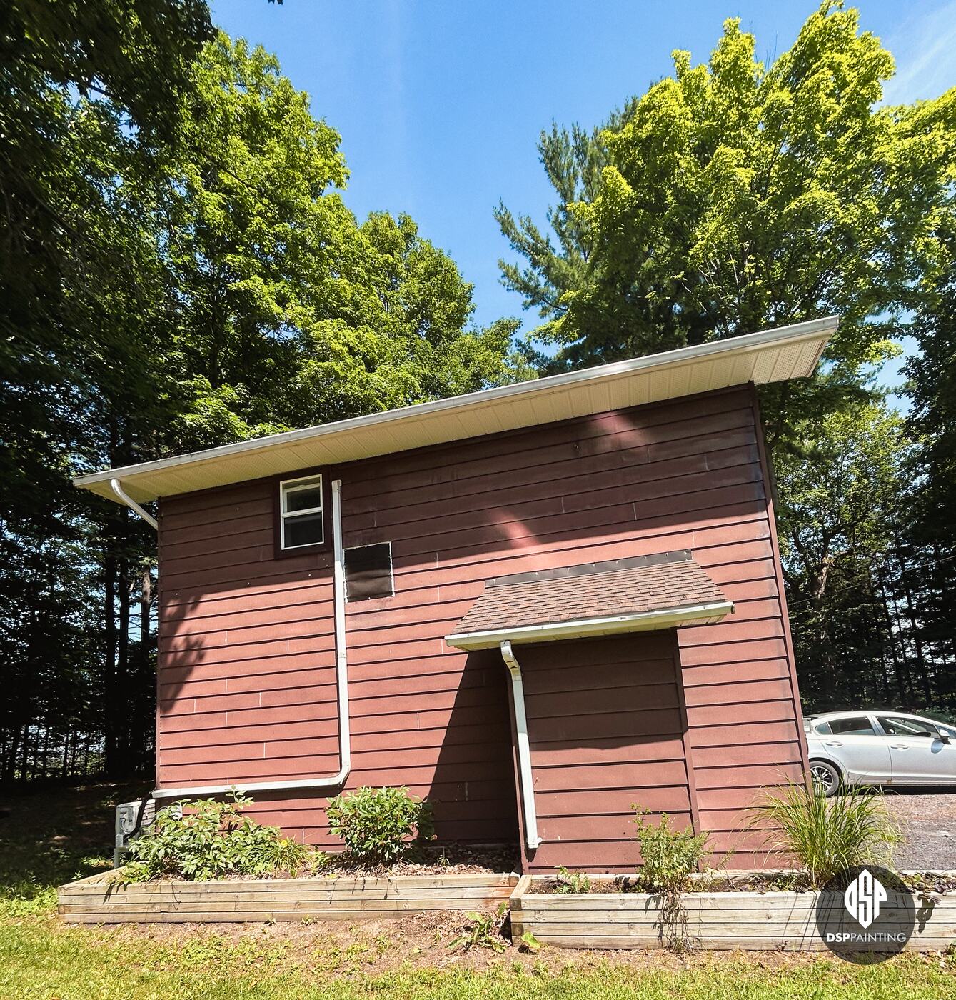 The side of the garage with its small shingled entry roof, red siding above raised garden beds