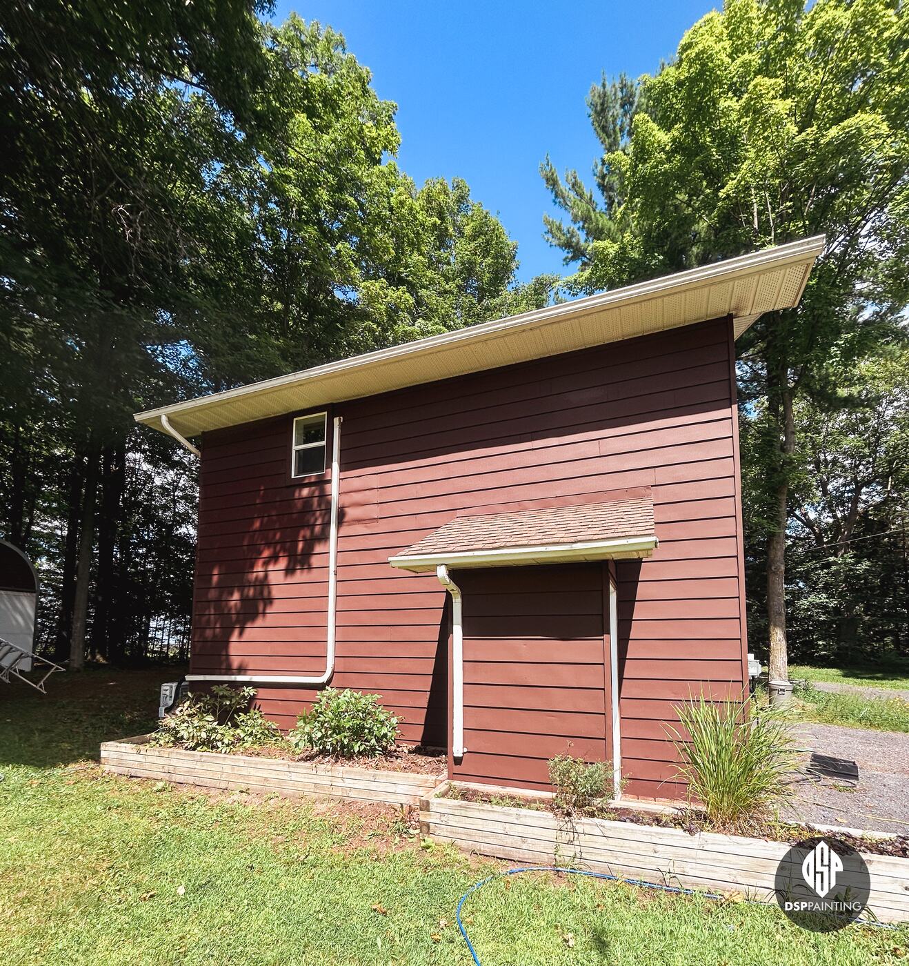 The shed-roof side of the garage, red siding above the garden beds and the small entry roof