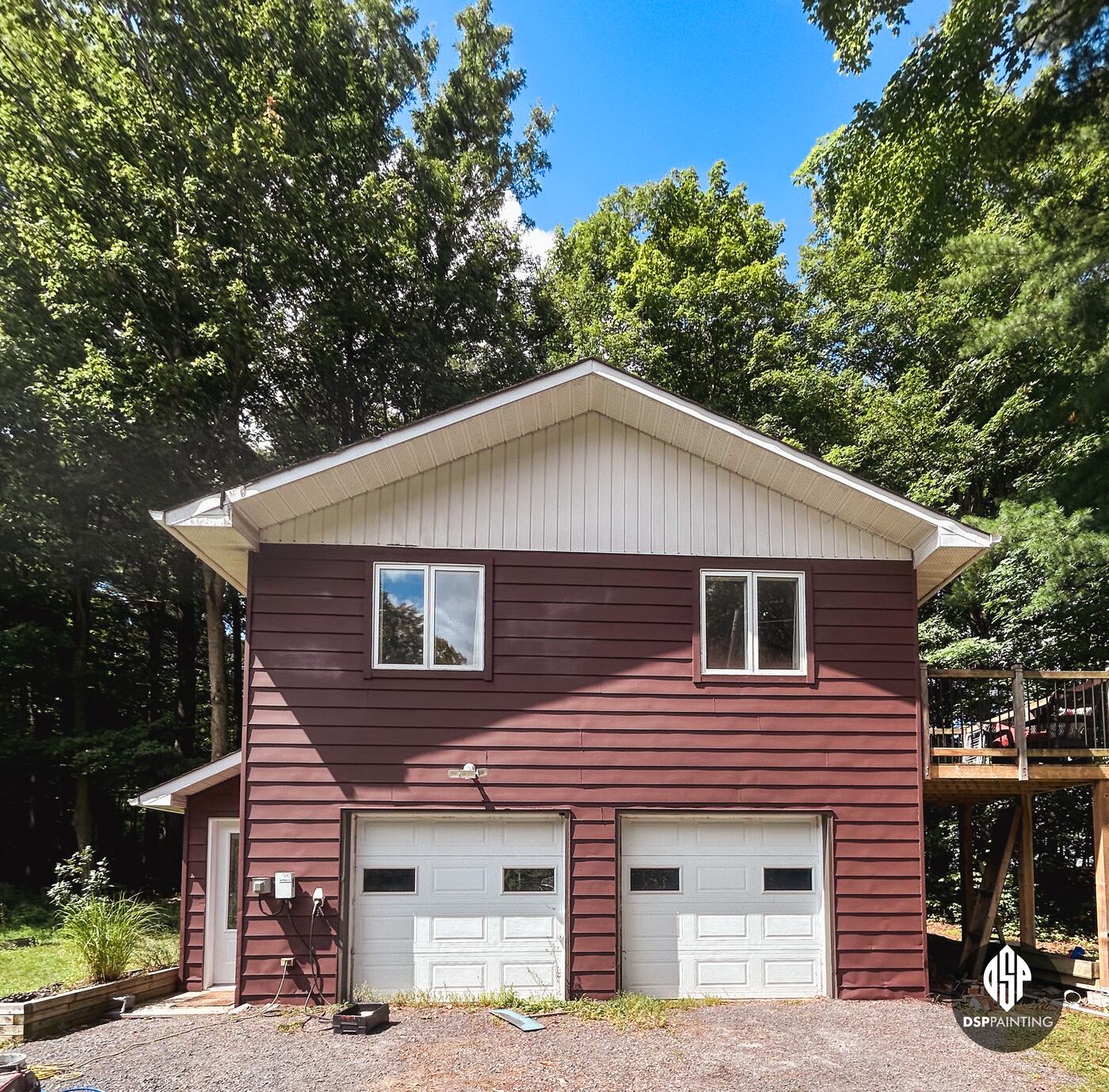 The two-storey garage, its lap siding painted a deep red-brown around two white overhead doors and the upstairs windows
