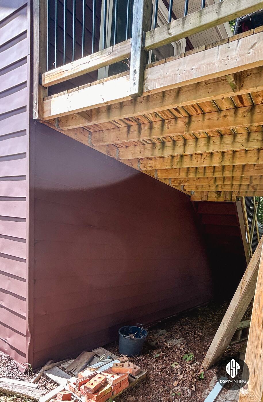 Red-brown siding carried under the second-floor deck, beside the deck’s wooden framing