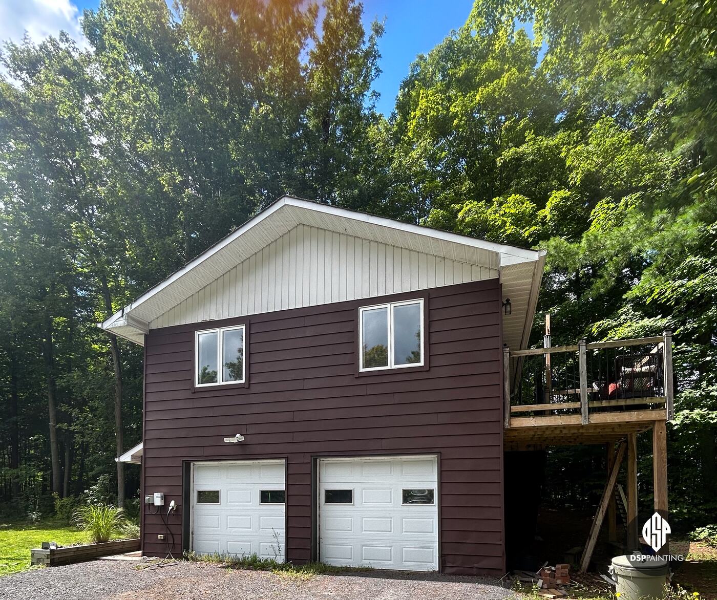 The front of the garage in shade, deep red-brown siding around the two overhead doors, with the deck to the right