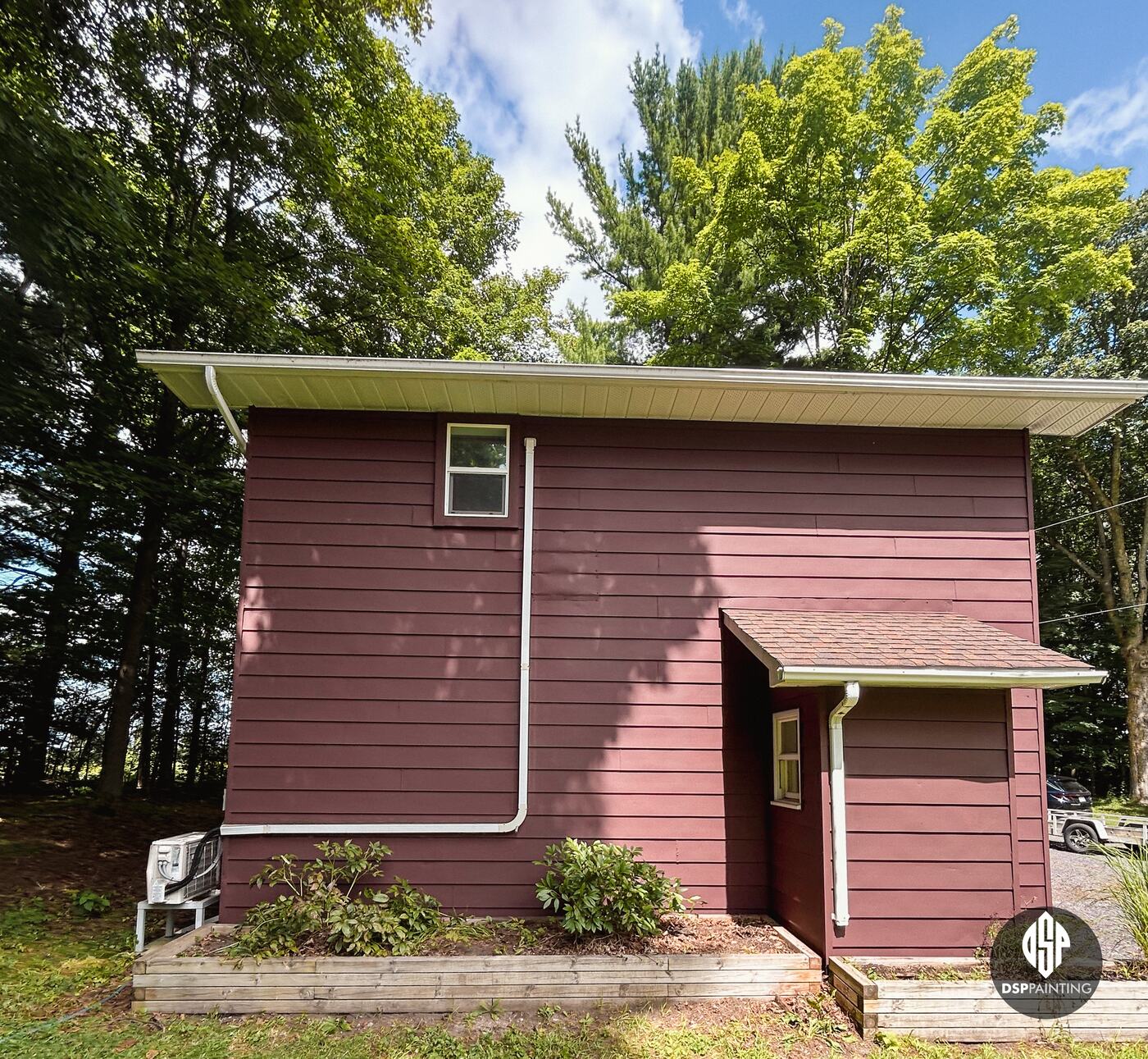 The side entry of the garage, red siding under the small shingled roof and white downspouts