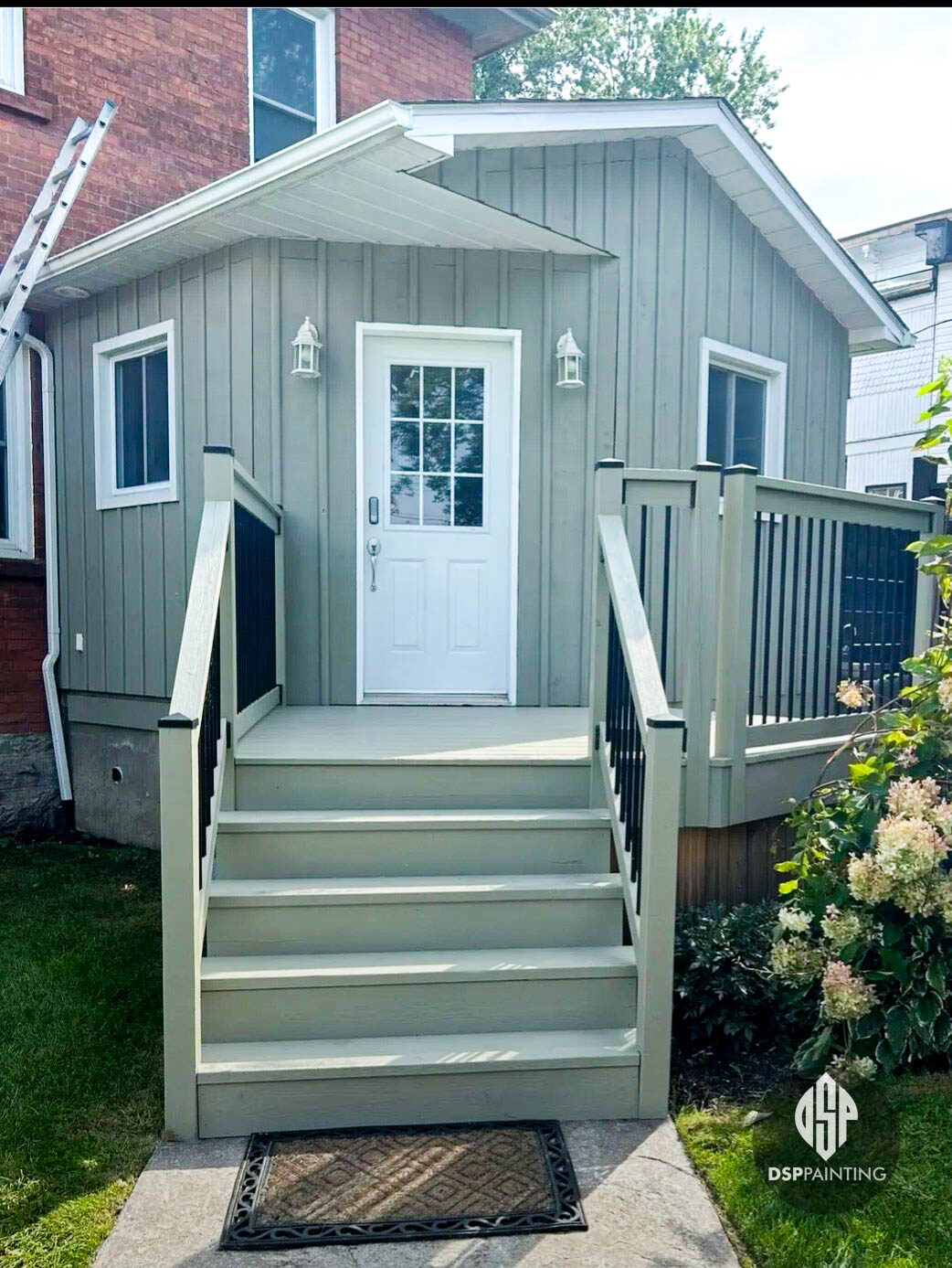 Side entrance of the house, board-and-batten siding in sage green with a white door and repainted deck