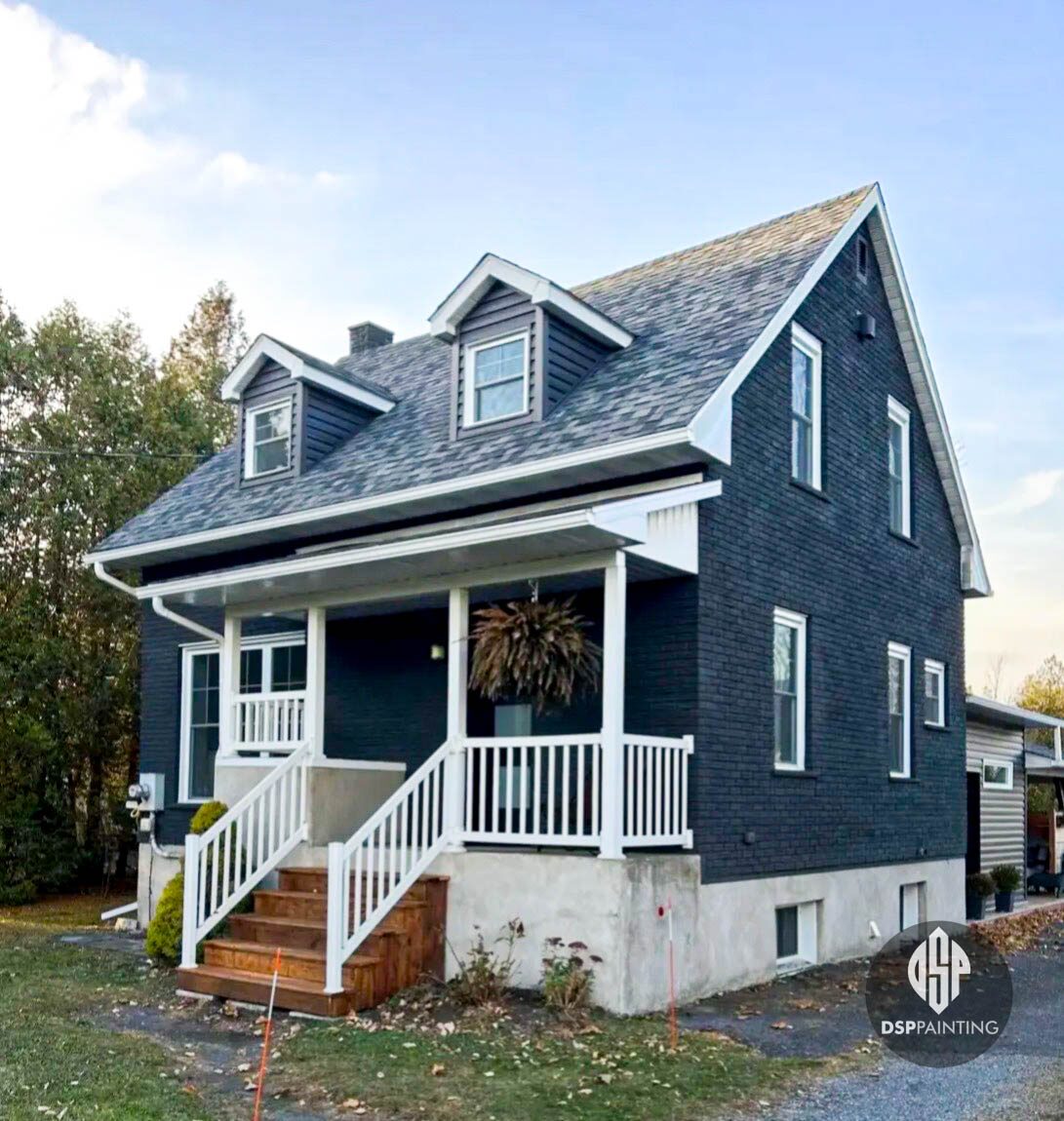 A country house with dark navy shingle siding and freshly painted white porch railings, posts and dormer trim