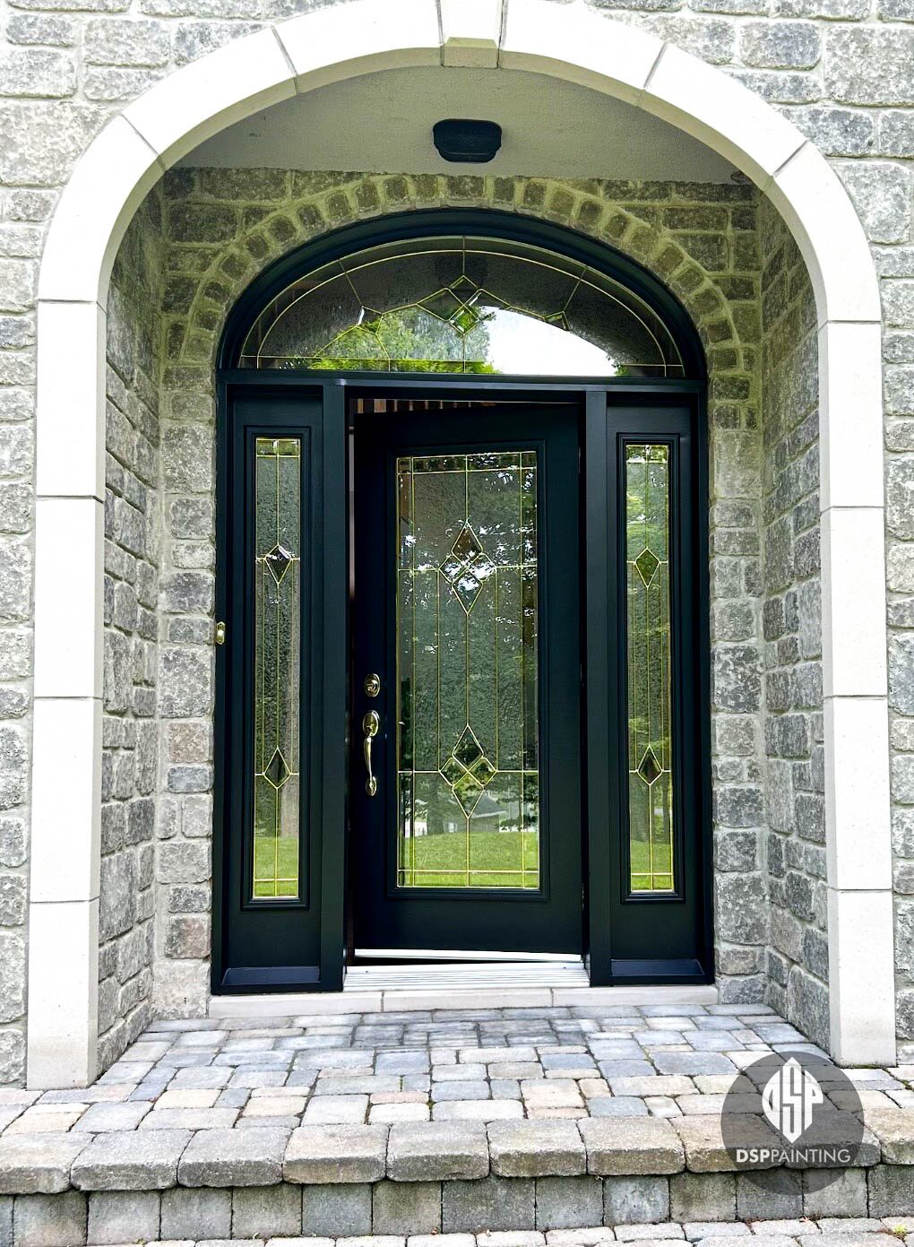 A stone-arched entryway with the front door, sidelights and transom frame painted gloss black