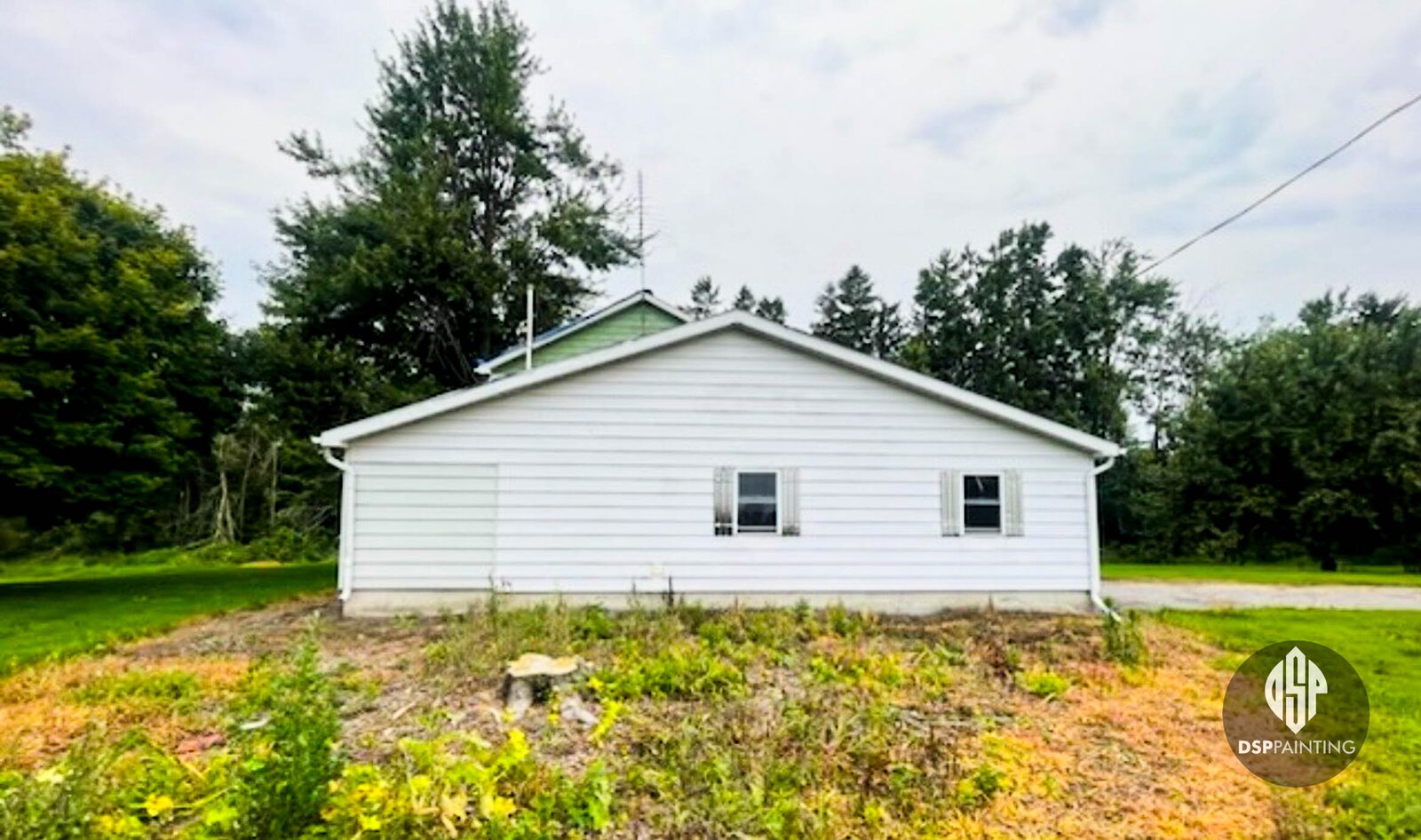 The house before painting, white vinyl siding and white shutters across the gable end