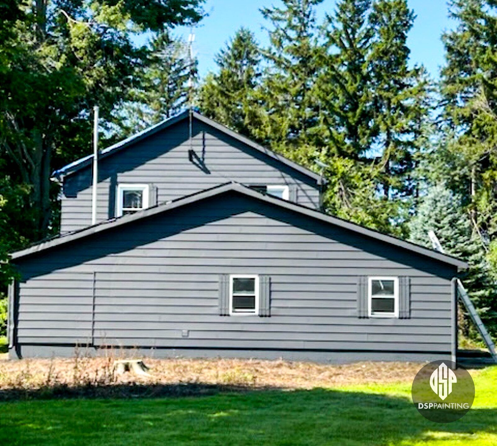 The gable end of a country house painted mid-grey, with black shutters and dark trim along the roofline