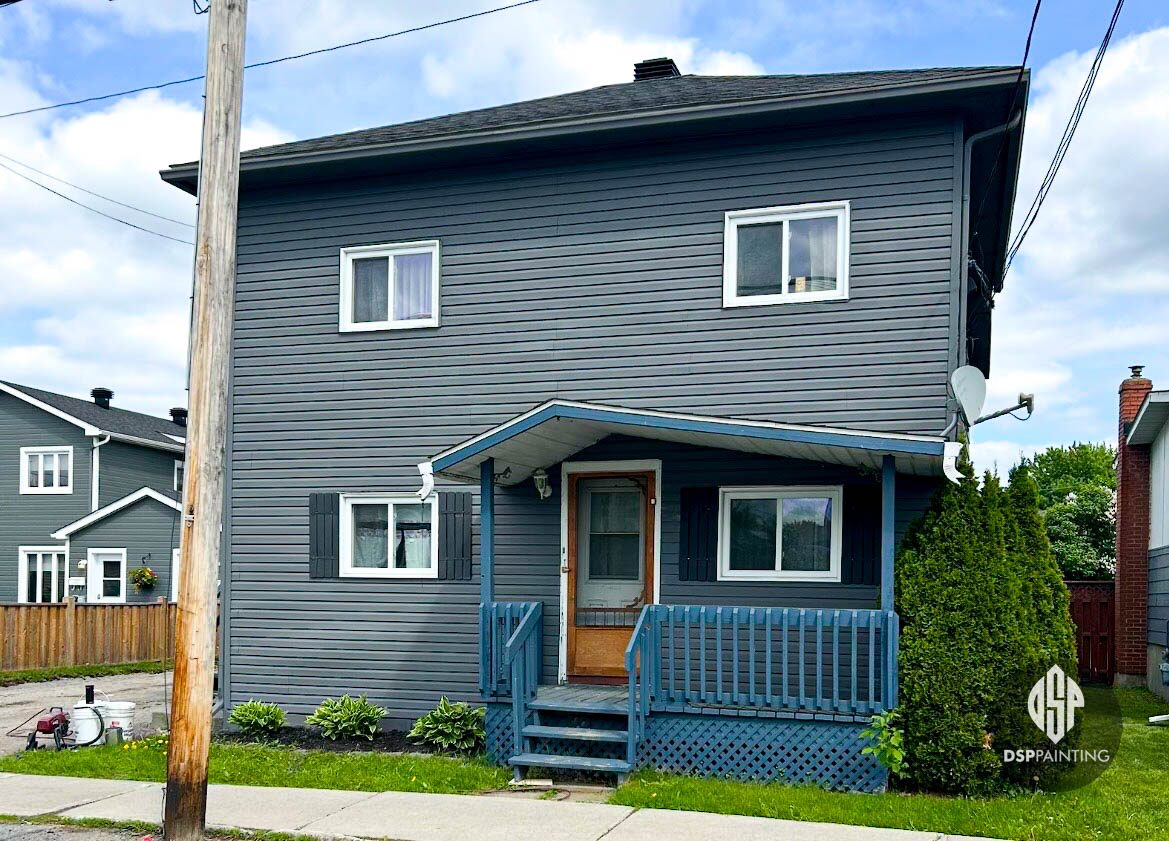 A two-storey clapboard house painted charcoal grey with white window trim and black shutters