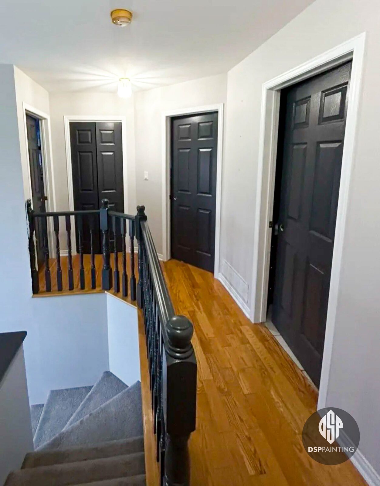 An upstairs landing painted in pale grey and white, with panel doors and a stair banister finished in gloss black