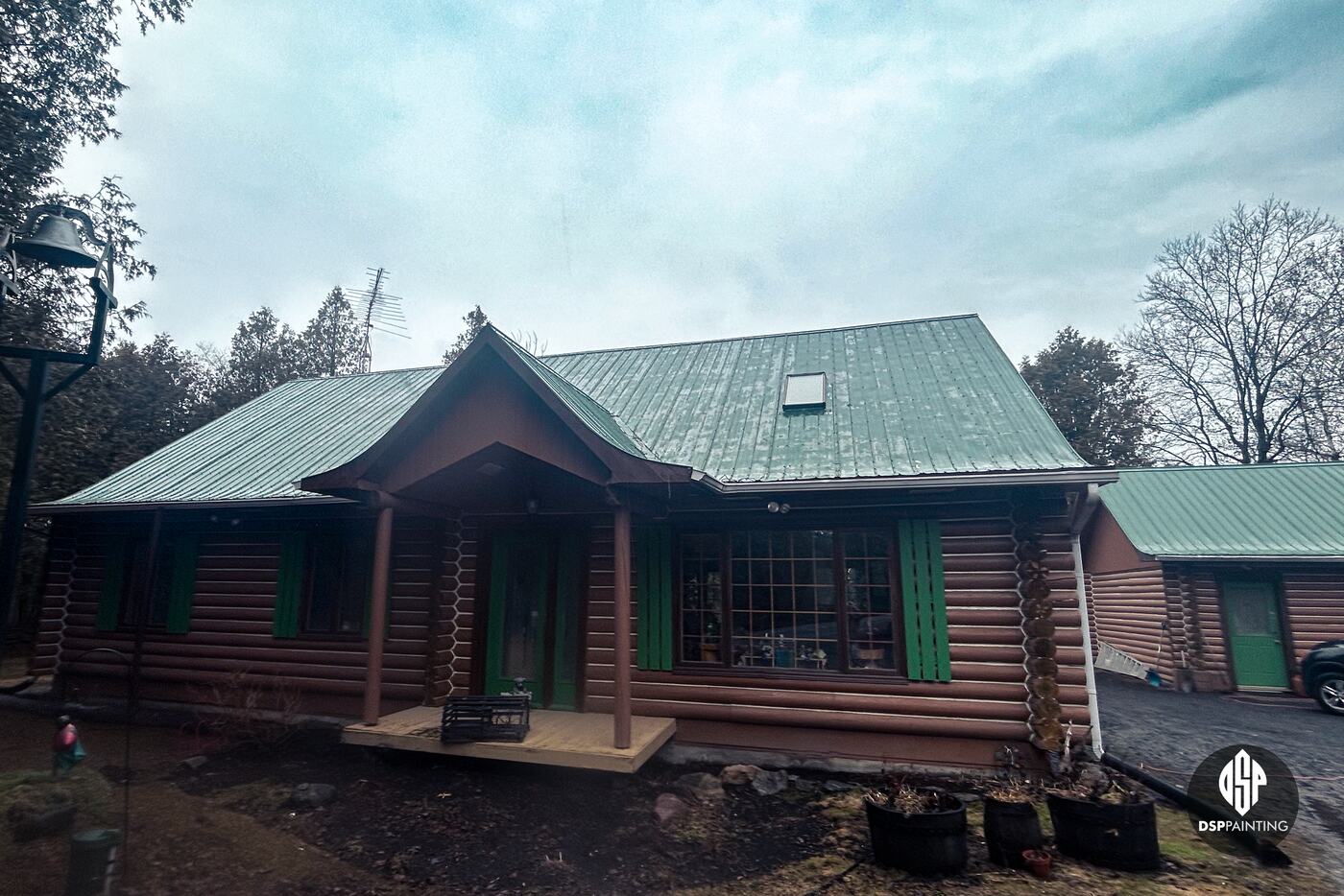 The front of the log house before the work, its green metal roof faded, with the log garage beside it