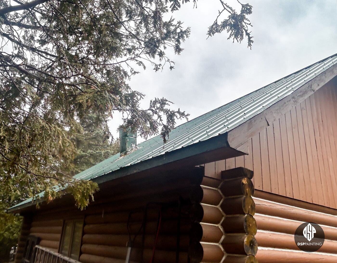 The roof edge before painting, dull green metal above the log walls and board gable