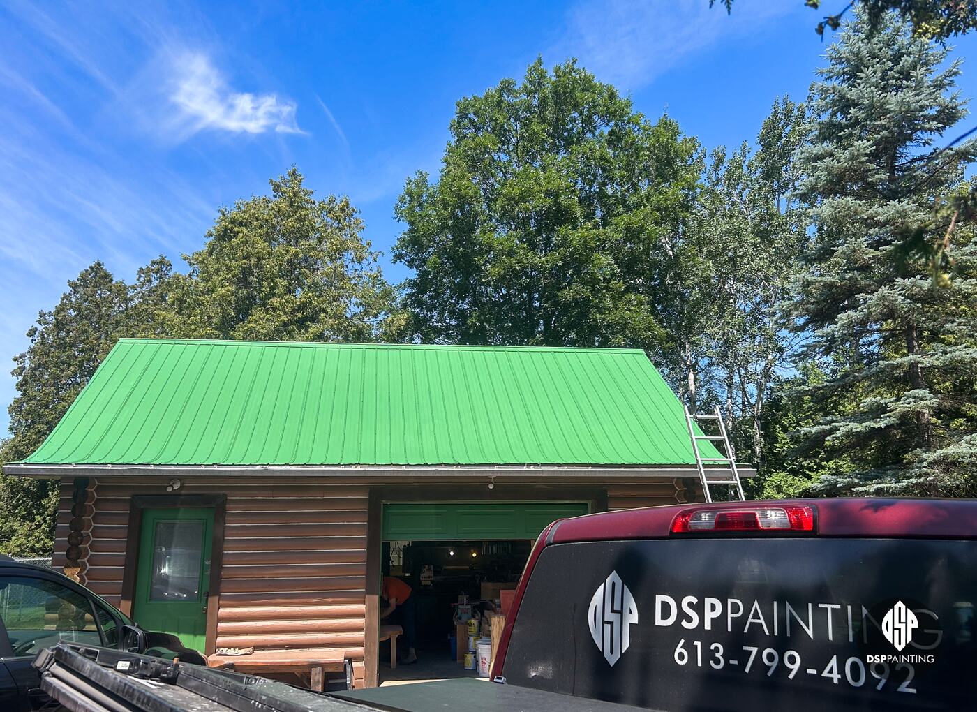 The log garage after painting, its metal roof bright green, with the DSP Painting truck in front