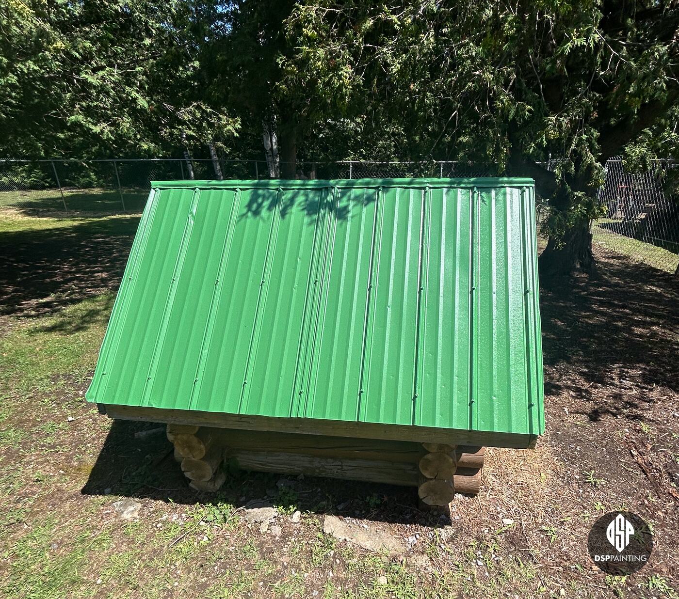 A small log-built shelter in the yard, its metal roof painted the same bright green