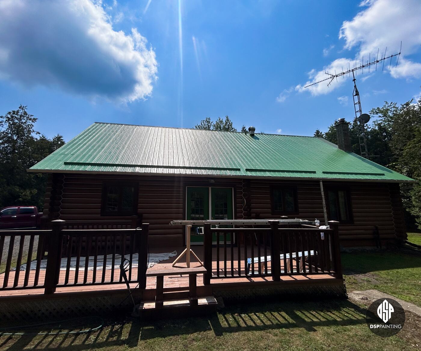The back of the log house, its long metal roof painted green above the deck