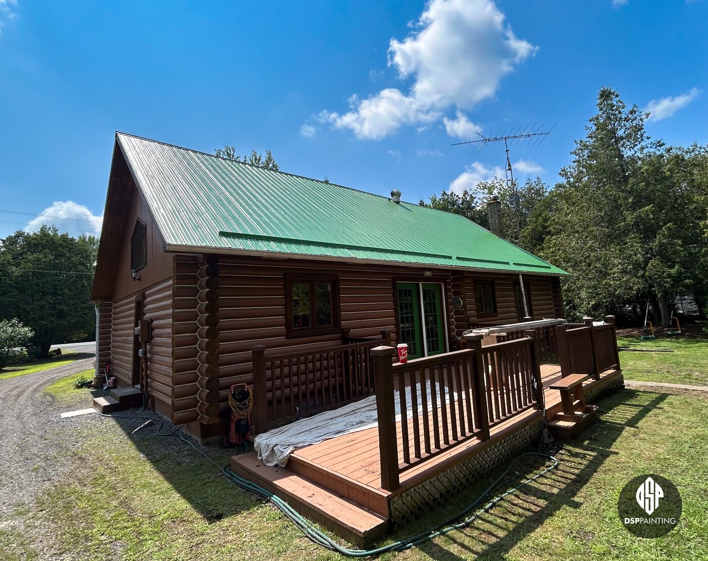 The back and gable end of the log house, the green roof running its full length above the deck