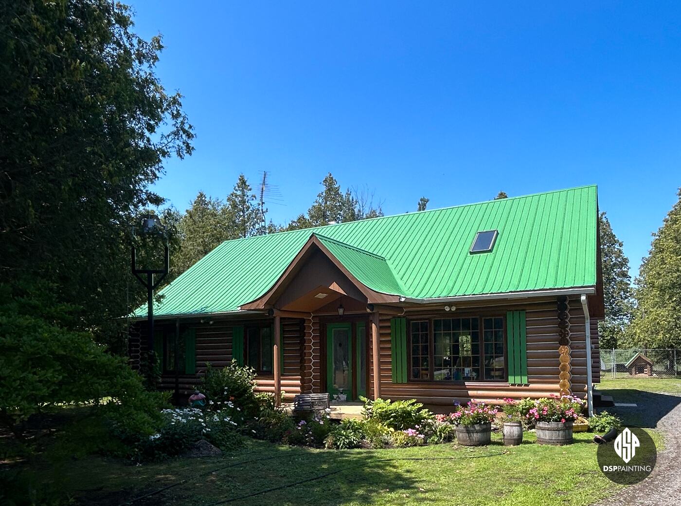 The front of the log house from the side, the bright green roof and skylight above the covered entry