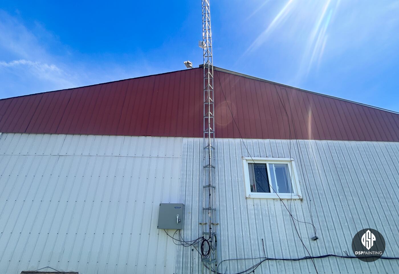 The rental building before the work, a red metal roof above weathered white steel siding