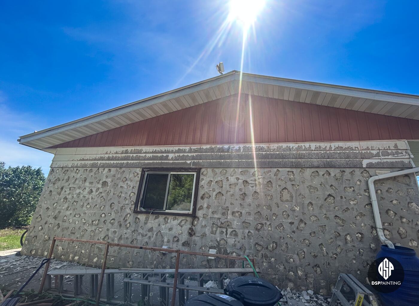 The stone-walled end of the building before the work, under a red metal gable