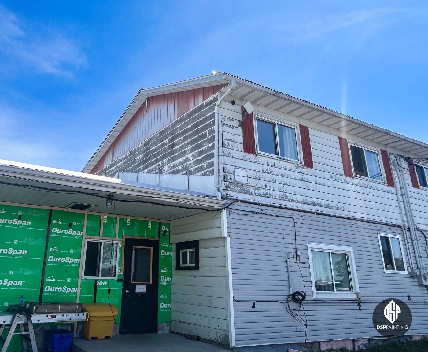 The two-storey part of the building before the work, a red gable and shutters above peeling white siding