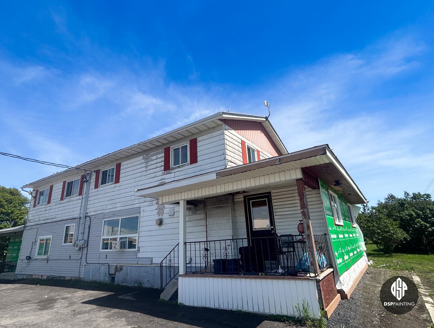 The front of the building before the work, red gables and shutters, white siding and the covered front porch