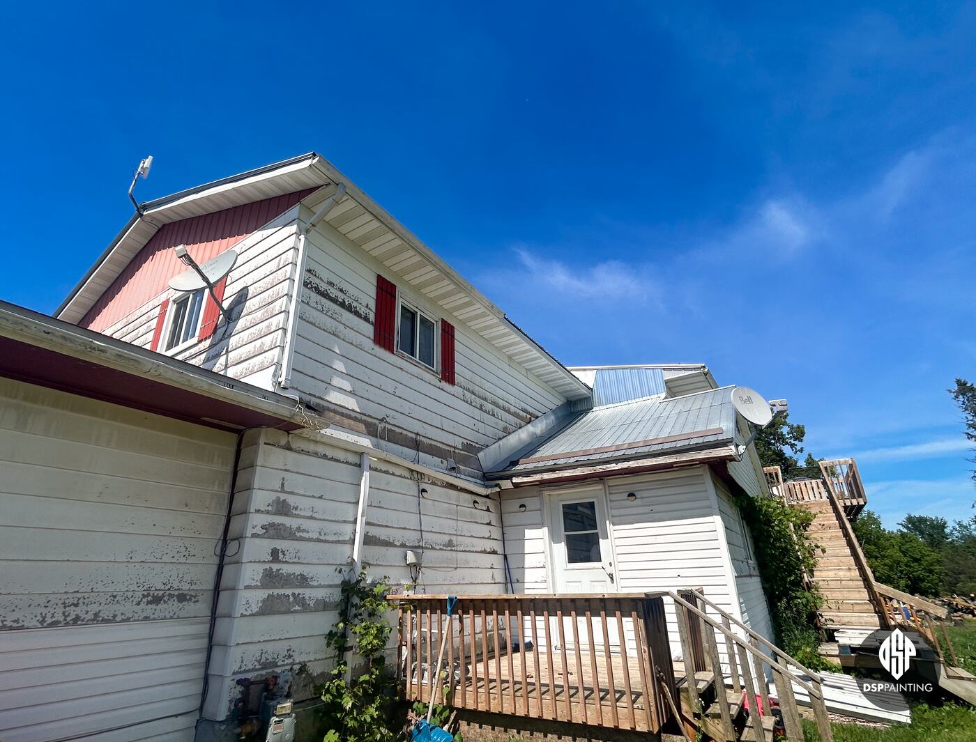 The back of the building before the work, paint peeling from the white siding under a red gable