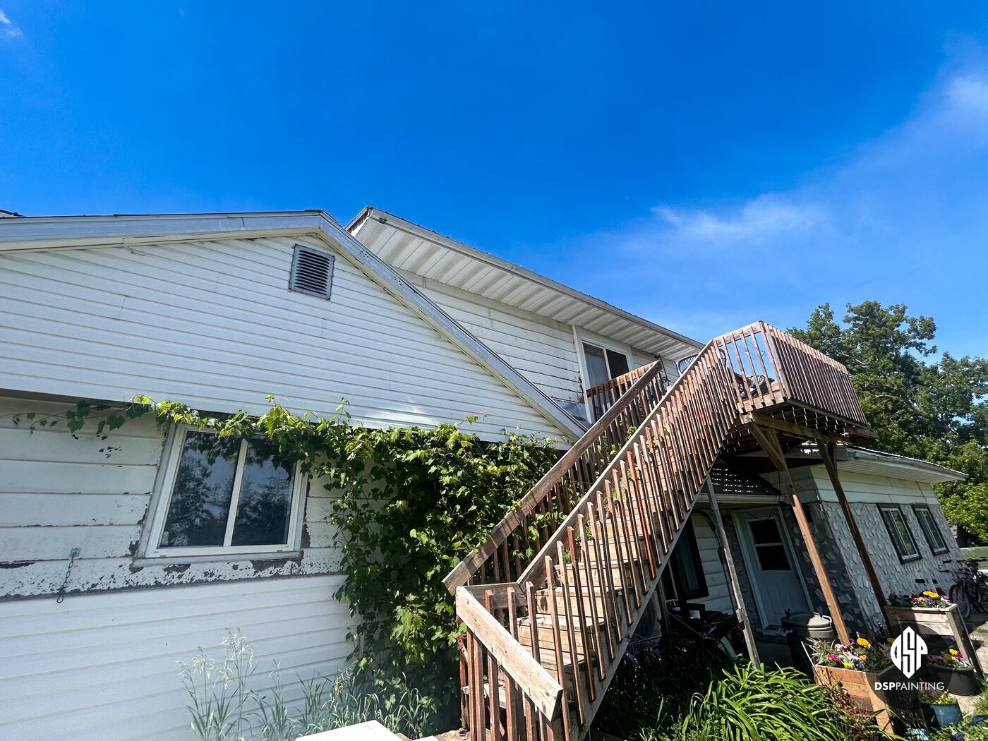 A side entrance before the work, peeling white siding beside the wooden exterior stairs