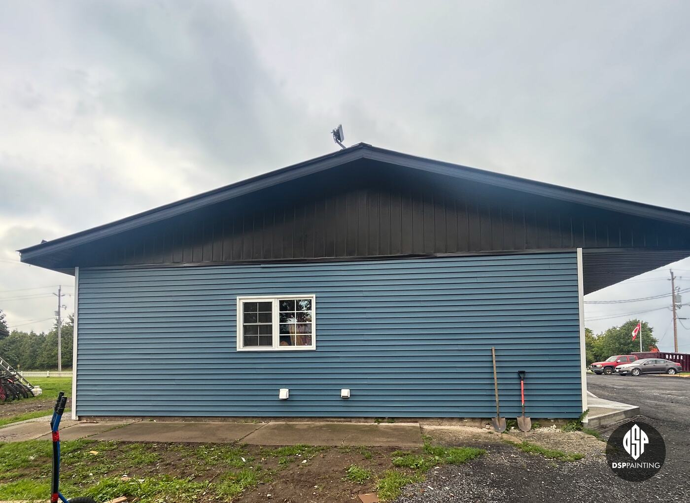 The end of the building after the work, the metal gable and roof edge painted black above blue siding