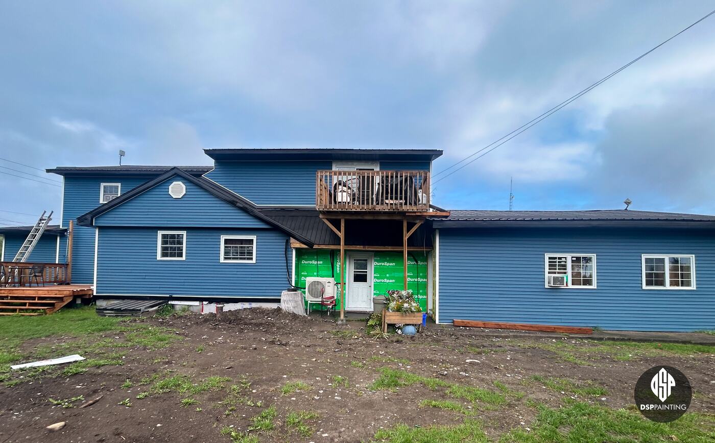The whole rental building from the back after the work, dark roofs above blue siding, with house wrap still showing on one entry