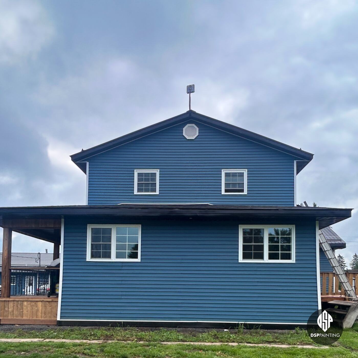 The rental building after the work, its roofs and roof edges dark charcoal above blue siding and white windows