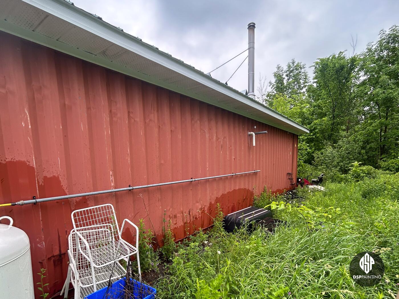 The long side of a container before painting, faded red steel with rust along the bottom