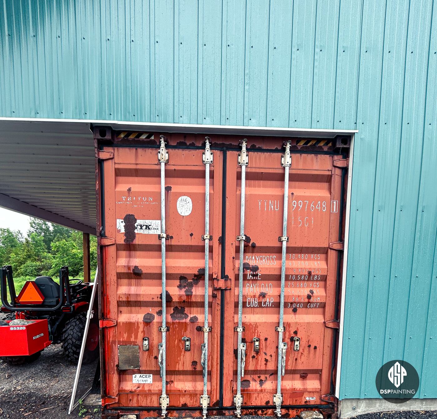 The doors of the second container before painting, red with rust spots, set into the teal building