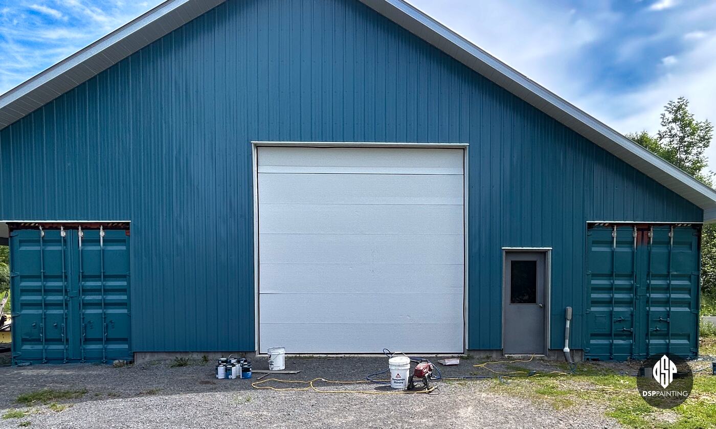 The end of the building with the work nearly done, both containers teal and paint cans still on the gravel