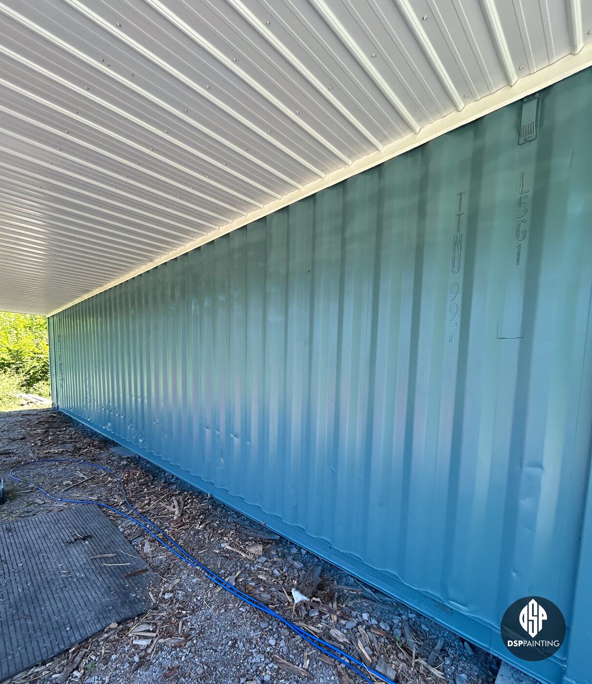 The long side of a container under the overhang after painting, teal from end to end
