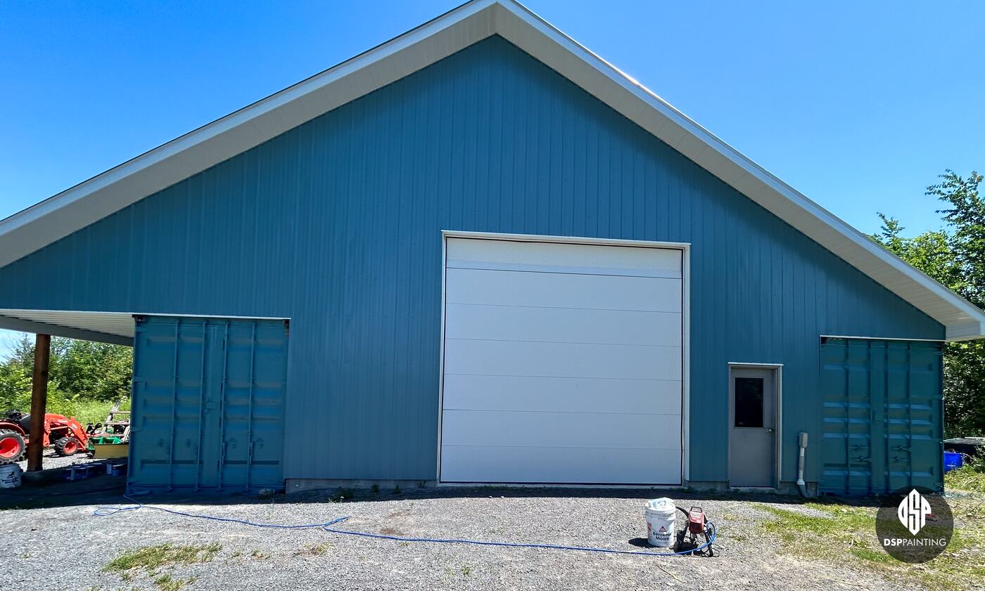 The building after painting, both shipping containers teal to match its steel siding, either side of the white overhead door